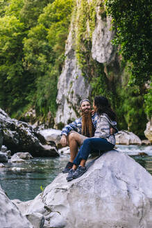 Glückliches junges Paar sitzt auf einem Felsen beim Wandern in den Picos De Europa, Asturien, Spanien - DGOF01716