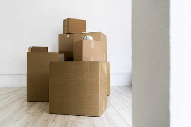 Brown cardboard boxes against wall in living room of new house - GIOF09685