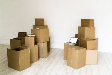 Stack of cardboard boxes with laptop in empty living room - GIOF09688