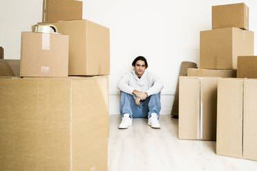 Mann sitzt inmitten von Kartons auf dem Boden im Wohnzimmer eines neuen Hauses - GIOF09690