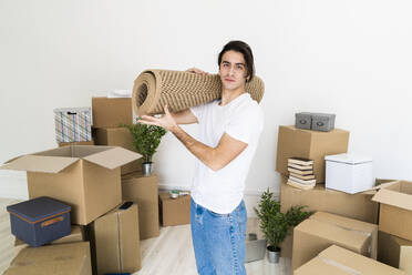 Young man carrying carpet on shoulder while relocating in new house - GIOF09714