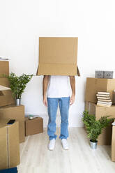 Man covering head with cardboard box while standing in new house  - GIOF09715