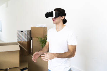 Lächelnder junger Mann mit Virtual-Reality-Simulator in neuer Wohnung - GIOF09717