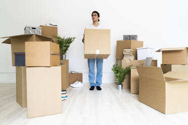 Young man holding big cardboard box while looking away in new house - GIOF09718