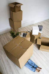 Young man hiding under cardboard box at new apartment - GIOF09724