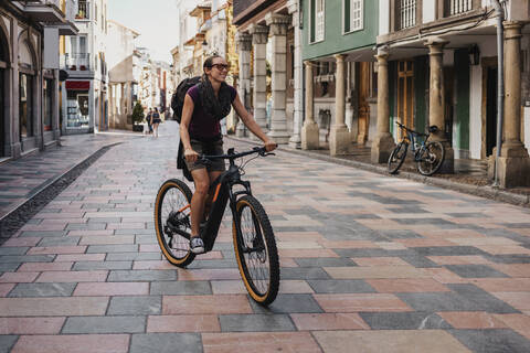 Woman with backpack riding electric mountain bike on street in city stock photo