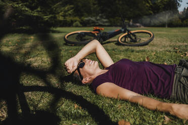 Frau liegt im Gras und ruht sich mit dem Mountainbike im Park aus - DMGF00306
