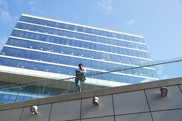 Businessman using smart phone while standing by glass railing against office building - PMF01545