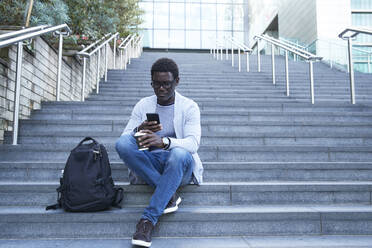 Unternehmer, der ein Mobiltelefon benutzt, während er einen Einwegbecher auf einer Treppe im Finanzviertel hält - PMF01547