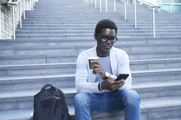 Male professional using mobile phone while holding disposable cup on staircase at financial district - PMF01549