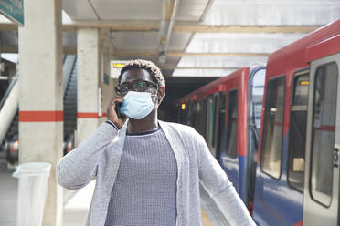 Male entrepreneur wearing protective face mask while talking on mobile phone at railroad station - PMF01562