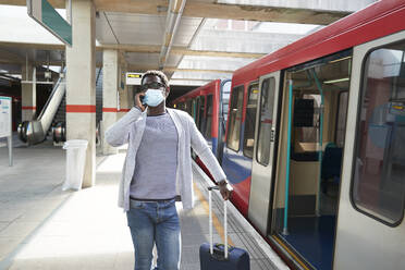 Älterer Geschäftsmann mit Schutzmaske telefoniert auf dem Bahnsteig - PMF01563