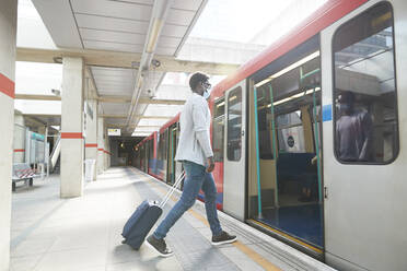 Männlicher Unternehmer auf Geschäftsreise beim Einsteigen in einen U-Bahn-Zug am Bahnhof während einer Pandemie - PMF01564