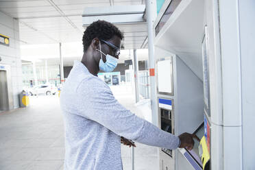 Älterer männlicher Berufstätiger, der während des Coronavirus einen Fahrkartenautomaten am Bahnhof benutzt - PMF01569