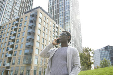 Männlicher Berufstätiger, der mit einem Mobiltelefon spricht, während er vor einem Bürogebäude in der Innenstadt steht - PMF01587