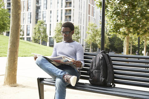 Mature male entrepreneur reading newspaper while sitting on bench in financial district stock photo