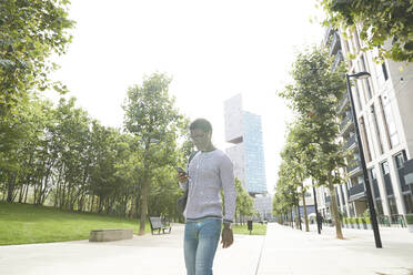 Male entrepreneur listening music through in-ear headphones while walking on footpath in city - PMF01593