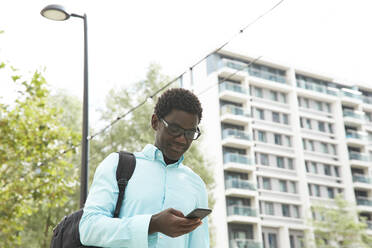 Lächelnder männlicher Unternehmer, der an einem sonnigen Tag in der Stadt ein Smartphone benutzt - PMF01606