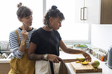 Frau schneidet Obst, während sie neben ihrer Freundin in der Küche steht - WPEF03587