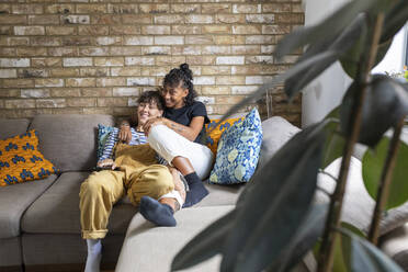 Happy lesbian couple watching tv while resting on sofa at home - WPEF03590