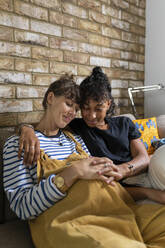 Lesbian couple sitting with hands clasped on stomach while sitting at home - WPEF03602