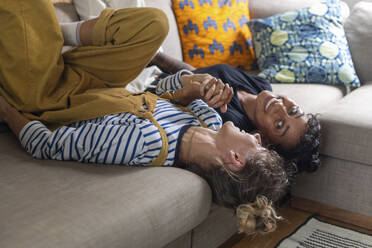Frau hält die Hand ihrer Freundin, während sie zu Hause auf dem Sofa liegt - WPEF03624