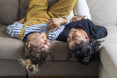 Lesbian couple holding hands while lying on sofa at home - WPEF03625