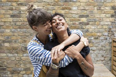 Happy woman embracing girlfriend while standing at back yard - WPEF03640