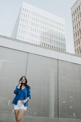 Unternehmerin, die mit ihrem Smartphone telefoniert, während sie an einem Gebäude steht - GMLF00817