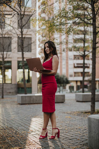Businesswoman using laptop while standing on footpath in city stock photo