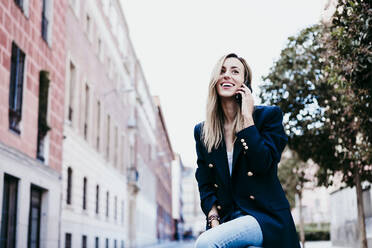 Beautiful woman smiling while talking on mobile phone in city - EBBF01548