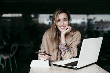 Beautiful businesswoman sitting with hand on chin at desk working in office - EBBF01557