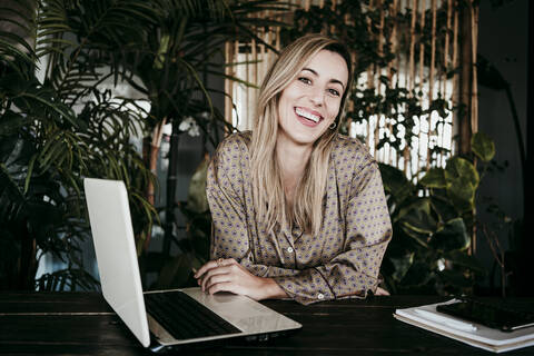 Happy female professional sitting with laptop at desk in office stock photo