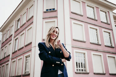 Smiling beautiful woman standing against building in city - EBBF01583