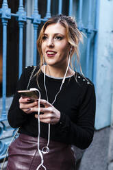 Lächelnde Frau, die ein Mobiltelefon benutzt, während sie am Fenster steht - JMPF00623