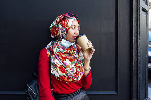 Muslimische Frau beim Kaffeetrinken an der schwarzen Wand während COVID-19 - JCMF01605