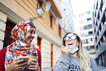 Fröhliche Freundinnen, die während der COVID-19 ihre Freizeit gemeinsam in der Stadt verbringen - JCMF01619