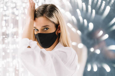 Young woman in protective face mask leaning on light wall - DAMF00623