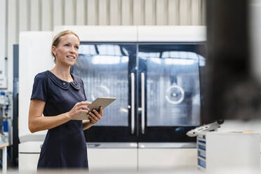 Lächelnde Geschäftsfrau, die ein digitales Tablet hält, während sie in einer Fabrik steht - DIGF13273