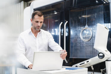 Männlicher Unternehmer arbeitet an einem Laptop in einer Fabrik - DIGF13282