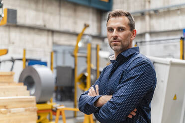 Selbstbewusster Geschäftsmann mit verschränkten Armen in der Industrie stehend - DIGF13303