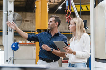 Female entrepreneur holding digital tablet looking away while male colleague gesturing in industry - DIGF13317