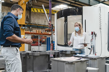 Unternehmerin und männlicher Kollege bei der Analyse von Maschinen in einer Fabrik während des Coronavirus - DIGF13320