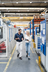 Male entrepreneur discussing while female colleague listening to him walking in factory - DIGF13323