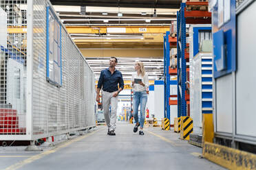 Geschäftsfrau und männlicher Kollege diskutieren beim Spaziergang in einer Fabrik - DIGF13324