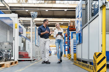 Female and male colleagues discussing while walking in factory - DIGF13325