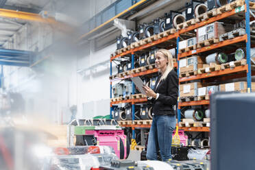 Blonde Unternehmerin hält ein digitales Tablet und schaut weg, während sie in einer Fabrik steht - DIGF13333