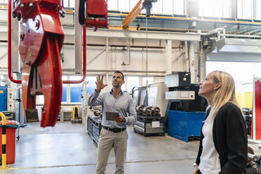 Male entrepreneur and female colleague examining claw machinery at factory - DIGF13341