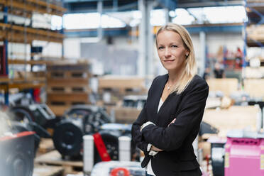 Selbstbewusste Geschäftsfrau mit verschränkten Armen in einer Fabrik stehend - DIGF13368