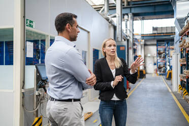 Male and female entrepreneurs discussing while standing in factory - DIGF13370
